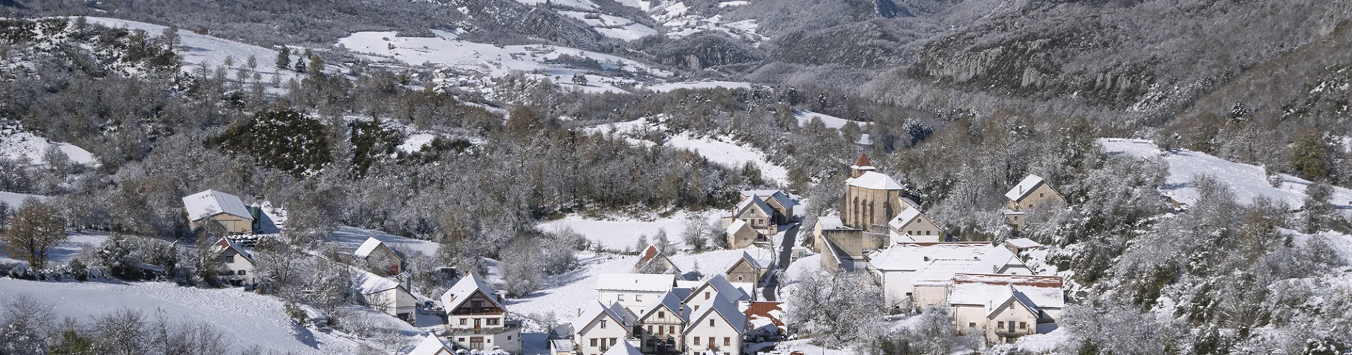 Pueblo de Abaurrea Baja en invierno con iglesia, casas de piedra blanca y montañas nevadas del Pirineo de fondo.
