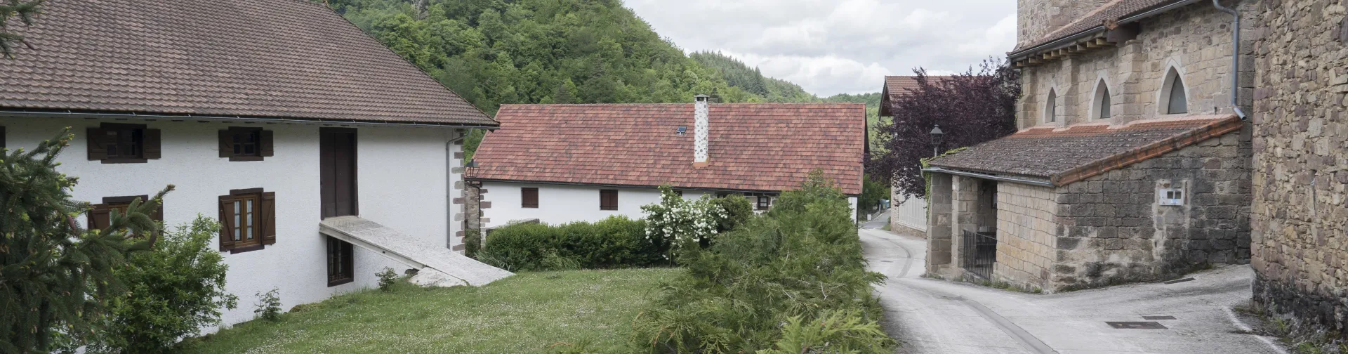 Pueblo de Azparren en el Pirineo navarro con caserios tradicionales de piedra blanca, iglesia con campanario y monte boscoso de fondo.