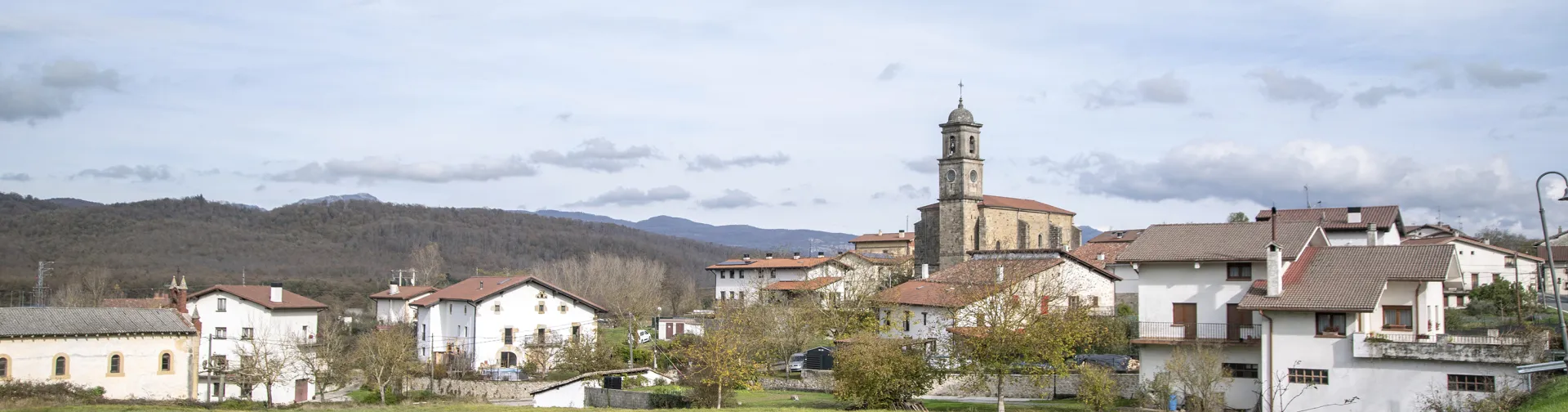 Pueblo de Bakaiku con iglesia de campanario rodeado de prados verdes y montañas boscosas al fondo.