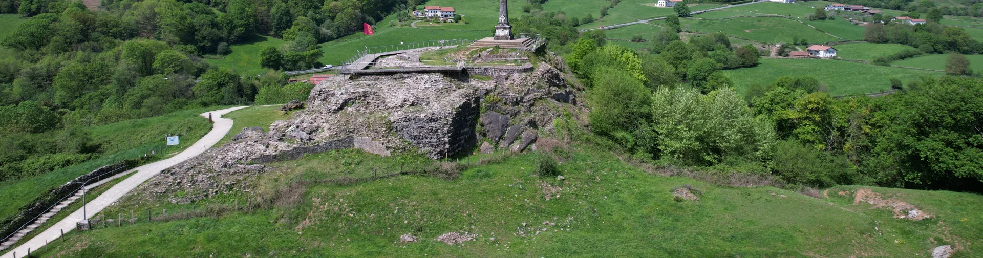 Castillo de Amaiur en valle de Baztan con monumento y paisaje de montañas verdes al fondo.