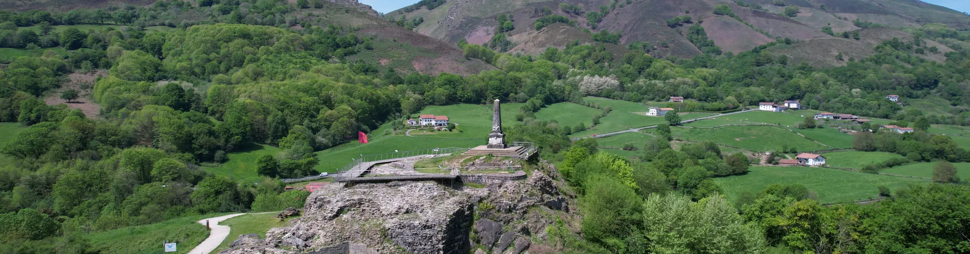 Castillo de Amaiur en valle de Baztan con monumento y paisaje de montañas verdes al fondo.