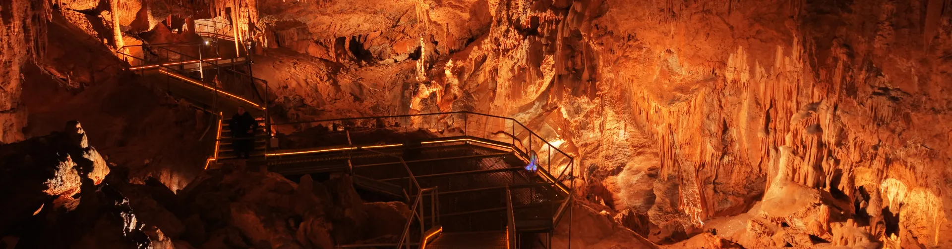 Cuevas de Mendukilo por dentro, con estalactitas y estalacmitas alumbradas con luces anaranjadas.