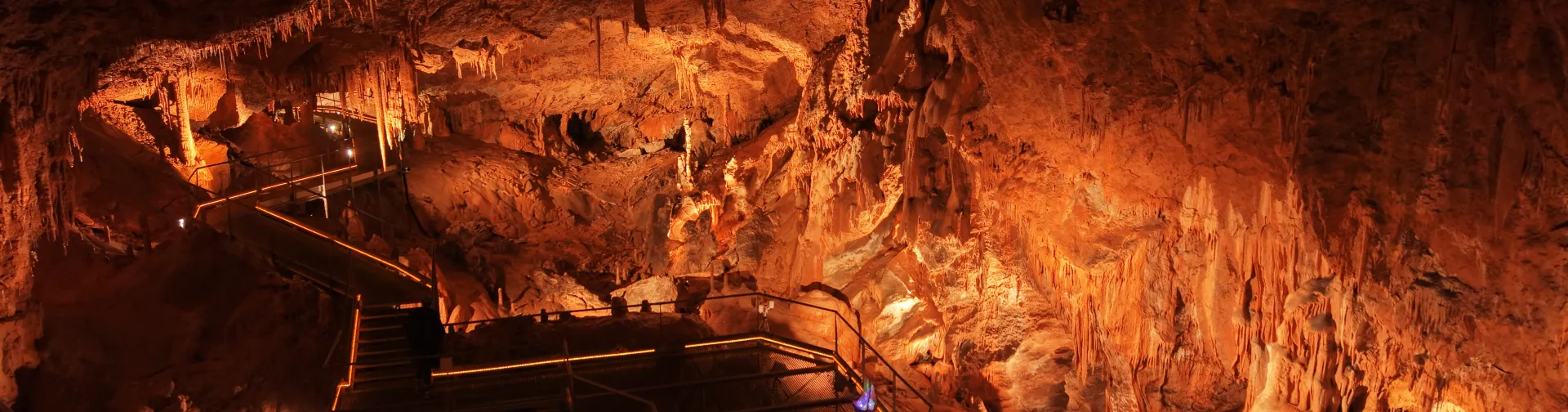 Cuevas de Mendukilo por dentro, con estalactitas y estalacmitas alumbradas con luces anaranjadas.