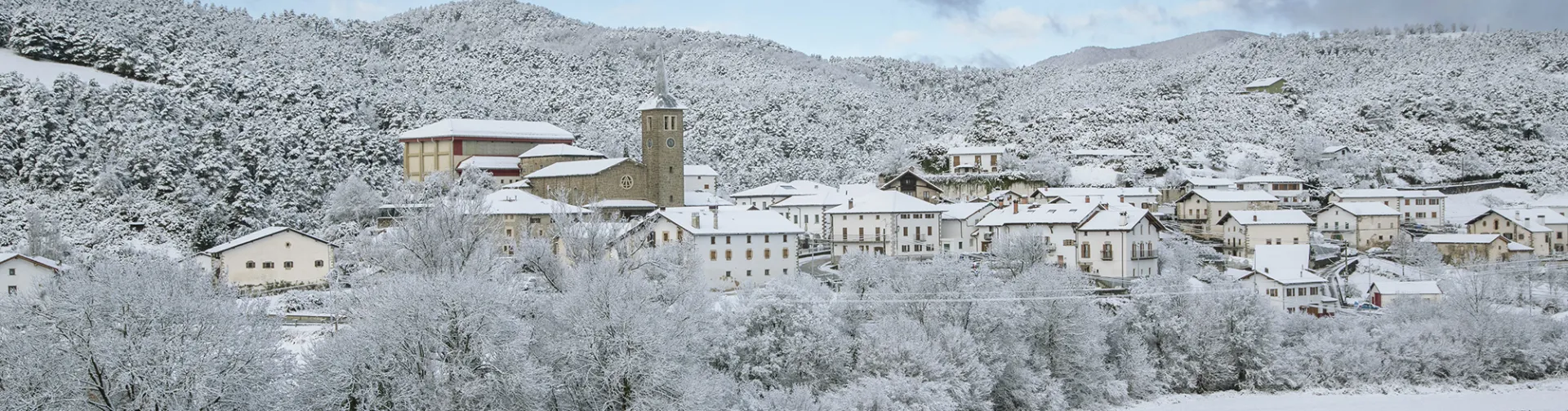 Pueblo de Erro bajo nieve con iglesia y casas de piedra tradicionales, rodeado de montañas nevadas en el Pirineo navarro.