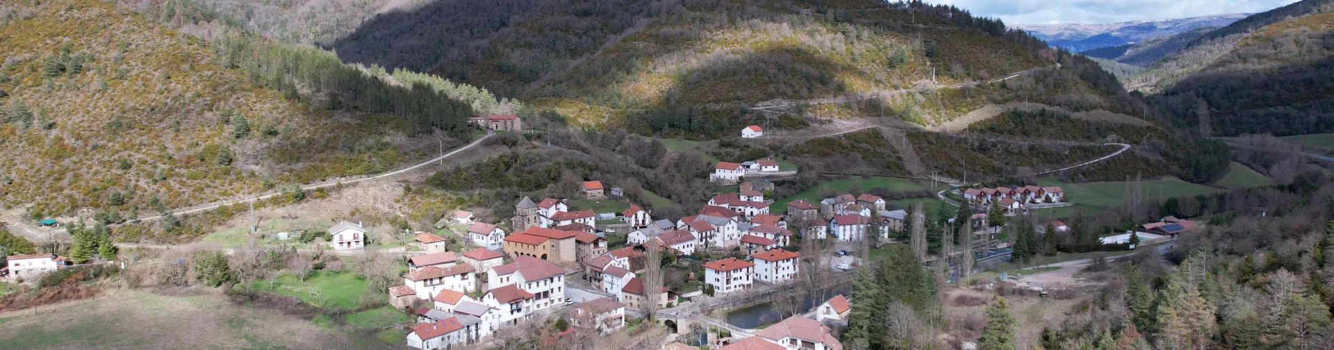 Vista aérea del pueblo de Esparza de Salazar rodeado de montañas boscosas y prados verdes en el valle pirenaico.