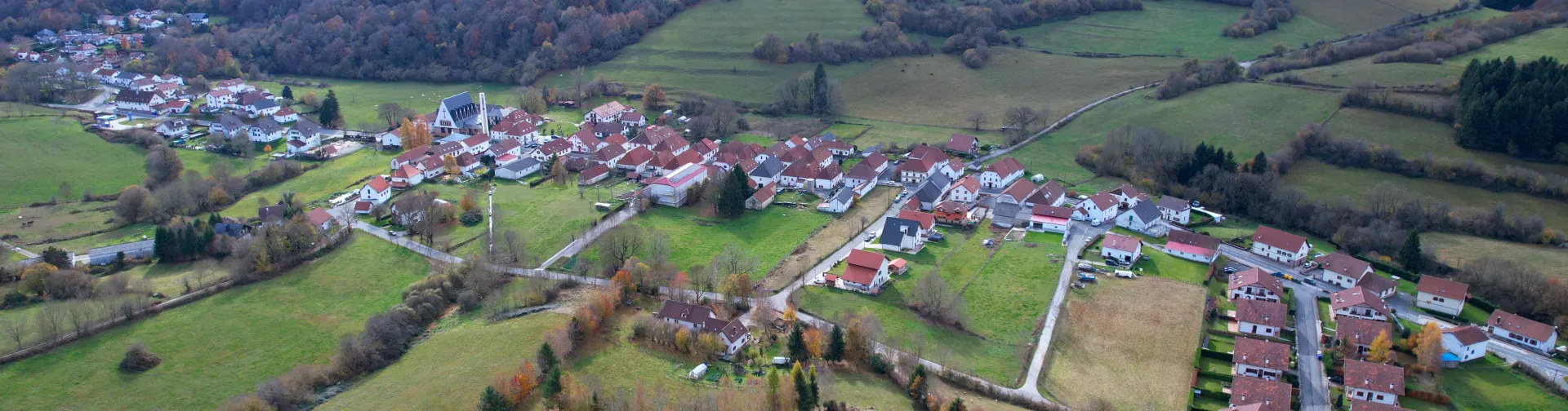 Vista aérea de Espinal en otoño tardío, pueblo pirenaico navarro rodeado de prados verdes y arquitectura tradicional de tejados rojos.