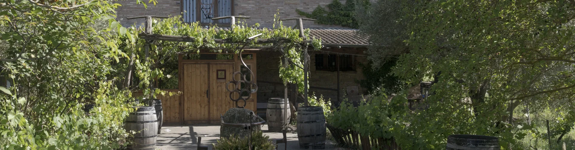 Entrada a bodega Azpea en Lumbier, con toneles de roble, vegetación y arquitectura rural tradicional.