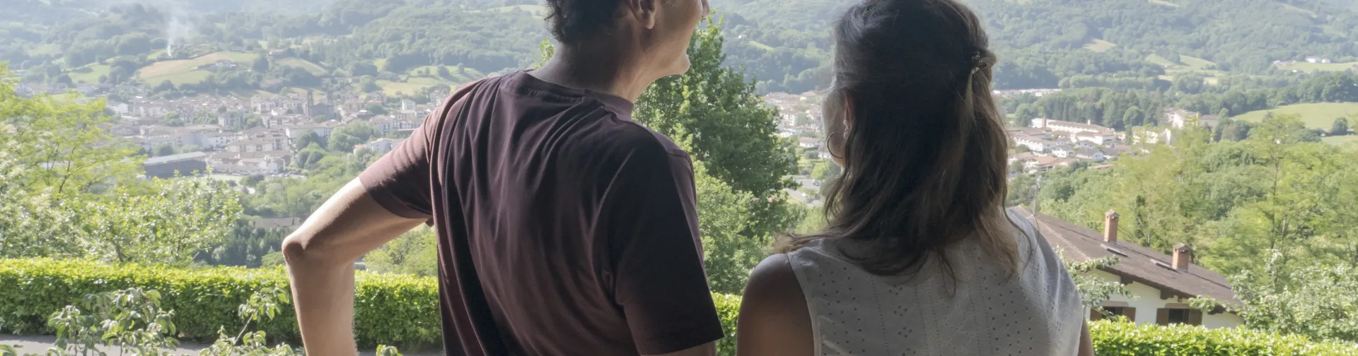 huespedes contemplan el Valle de Baztan desde un balcon de Markulluko Borda, con pueblo de Elizondo y montes verdes al fondo.