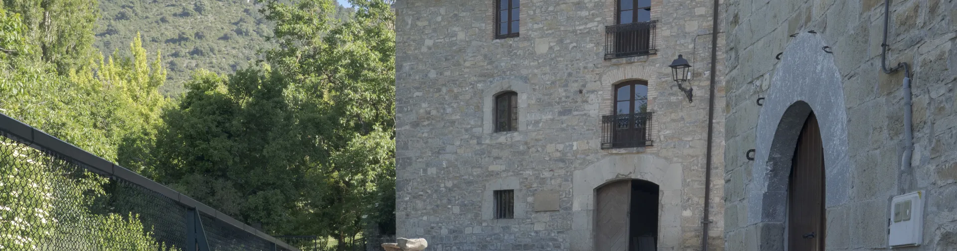 Casa Perotx Enea en Adoain, casa de piedra en la Comarca de Sangüesa, con cortados calizos al fondo y vegetación.