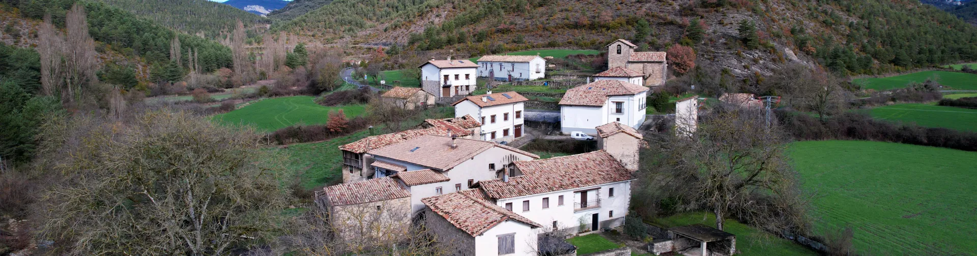 Valle de Gallues con casas de piedra tradicionales, prados verdes y montañas boscosas al fondo.