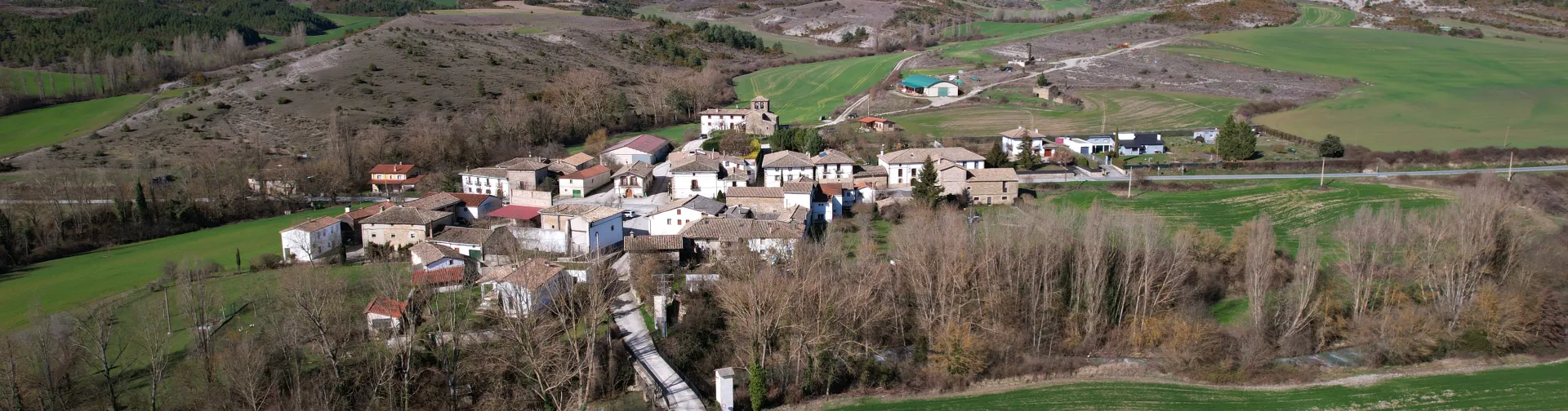 Pueblo de Urraul Bajo visto desde el aire con castillo medieval, caseríos dispersos y campos verdes.