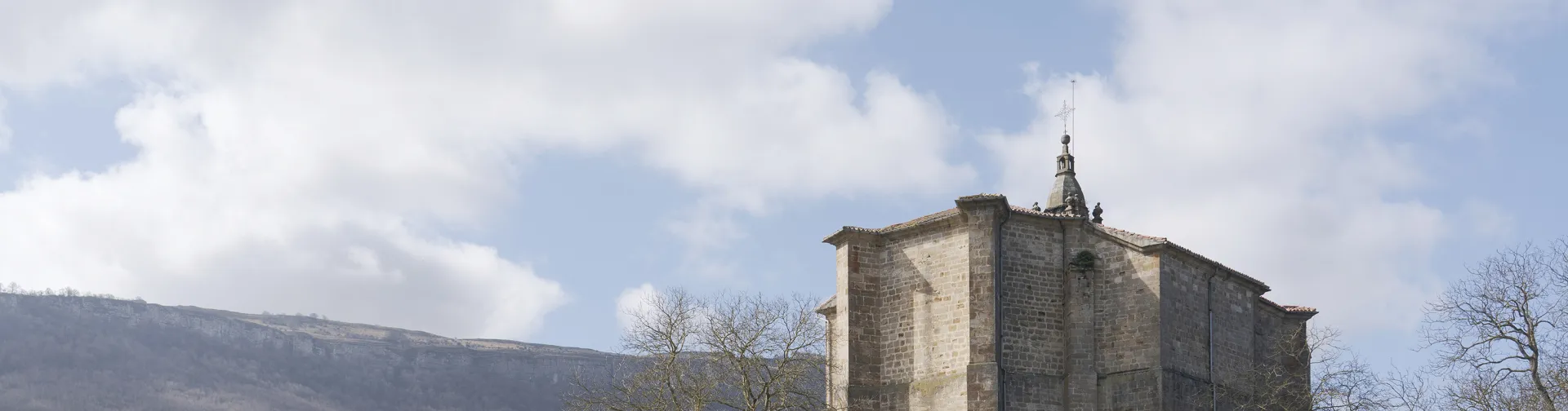 Iglesia de piedra con campanario en Iturmendi, rodeada de prados y montes.