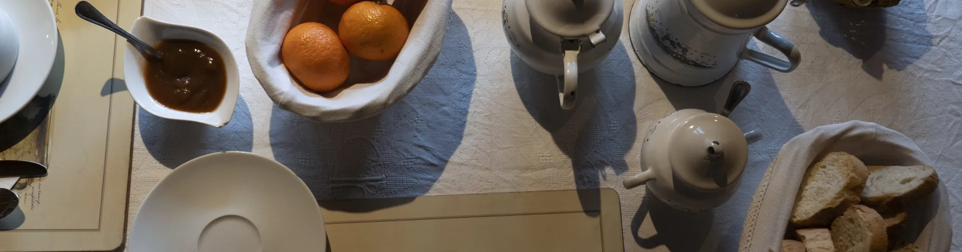 Mesa de desayuno con naranjas, pan tostado, queso, chocolate y vajilla de cerámica en alojamiento rural de Isaba.