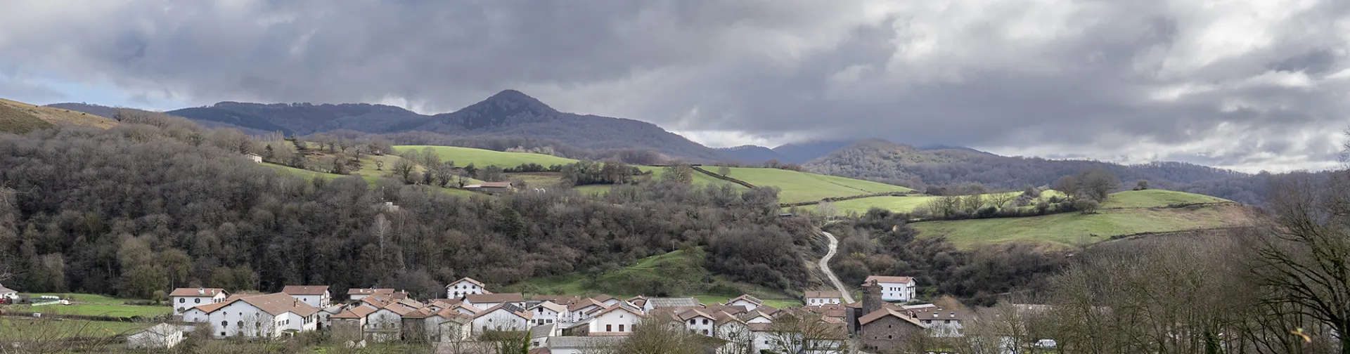 Pueblo de Lantz rodeado de prados verdes y bosques con montañas al fondo bajo cielo nublado.