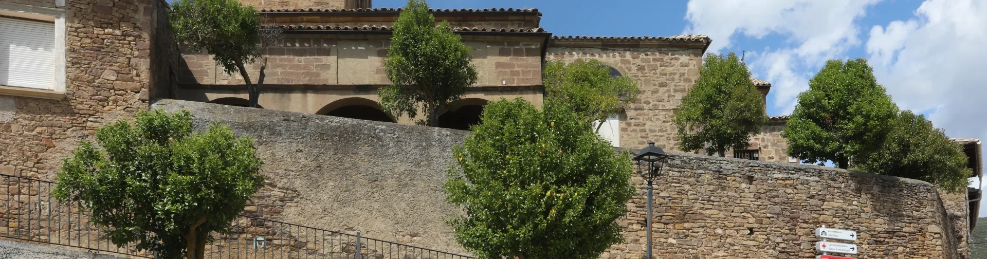 Iglesia rural de Liédena con torre campanario de piedra, arcos románicos y vegetación.