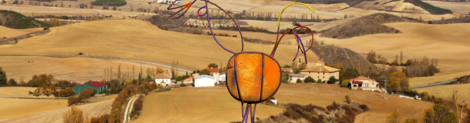 Escultura de metal colorida sobre roca con vista panorámica al valle agrícola desde la Peña Izaga.