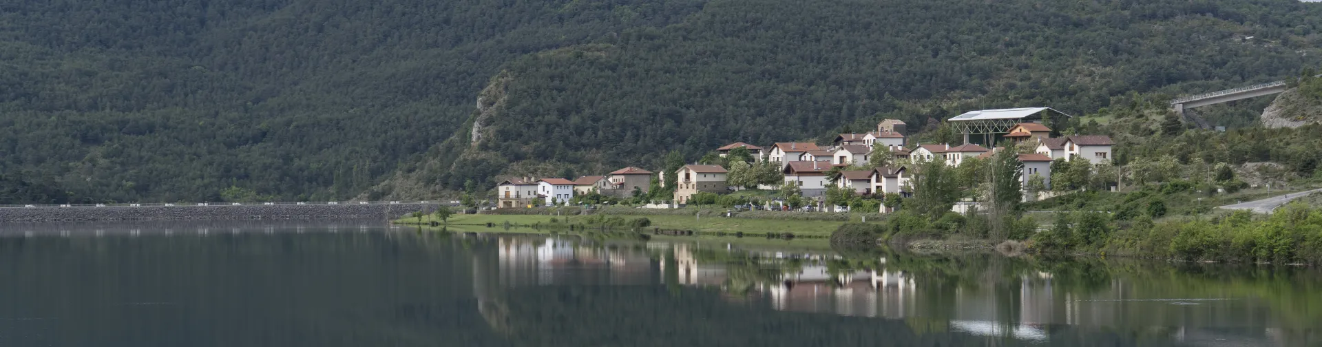 Vista general del pueblo de Nagore al lado del pantano de nagore, con monte boscoso al fondo.