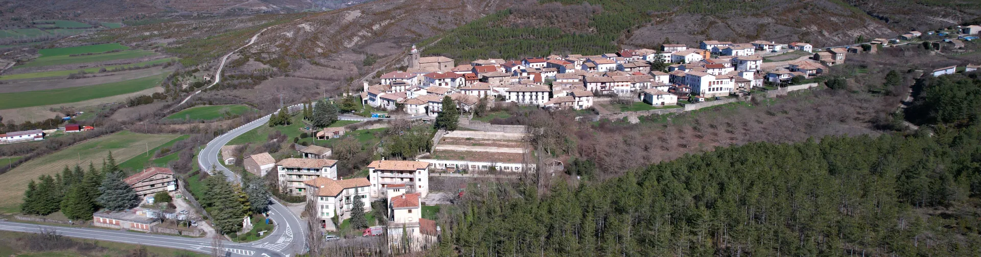 Vista aérea de Navascués rodeado de bosques y montañas del Pirineo navarro con carretera de acceso.