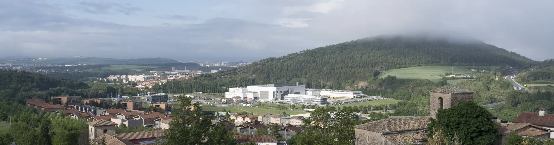 Vista panorámica del pueblo de Olloki con prado verde en primer plano y monte boscoso al fondo.