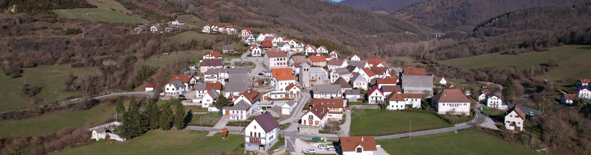 Vista aérea de Orbaizeta con casas de tejados rojos y blancos rodeadas de montes boscosos en el Pirineo de Navarra.