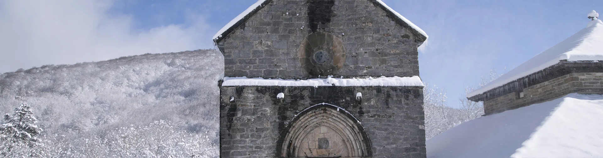Capilla de piedra medieval con campanario en Orreaga rodeada de nieve y montañas nevadas de fondo.