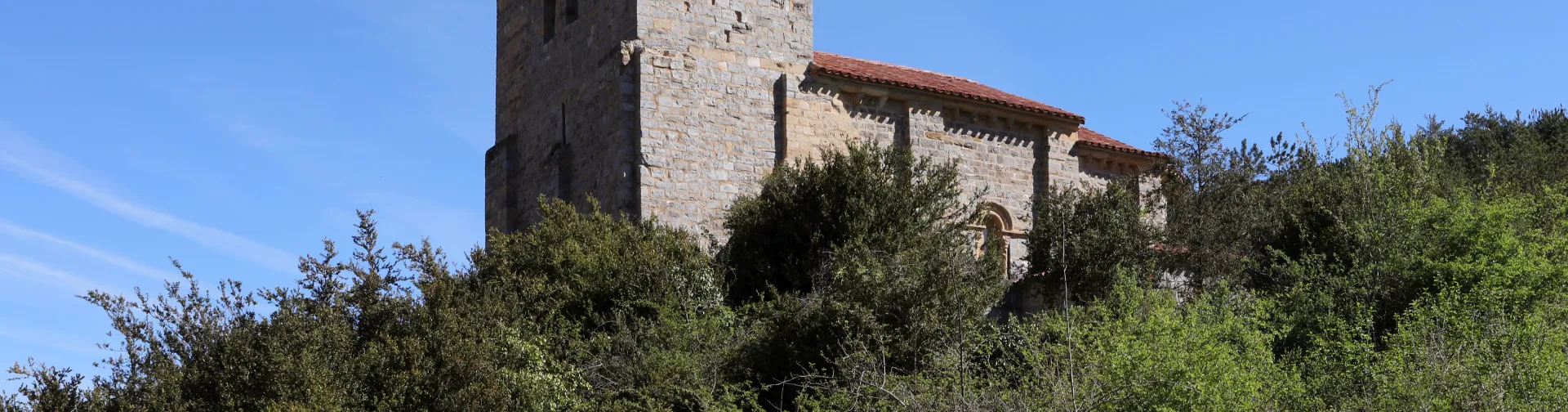 Ermita románica de Santa María de Arce en el Pirineo navarro, iglesia de piedra con torre campanario cuadrada sobre vegetación de transición.