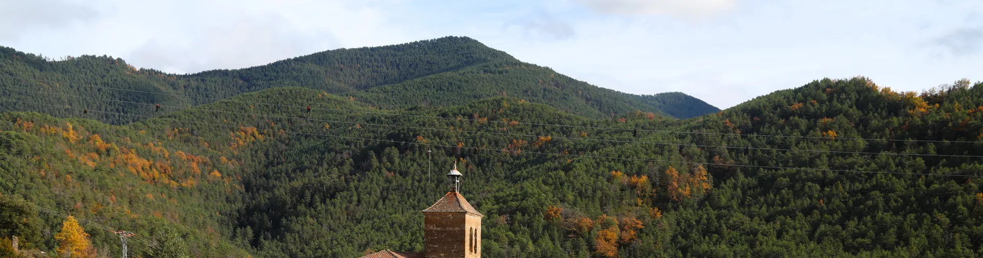 Pueblo de Roncal con iglesia, casas de piedra y tejados rojos rodeadas de bosque pirenaico en otoño.