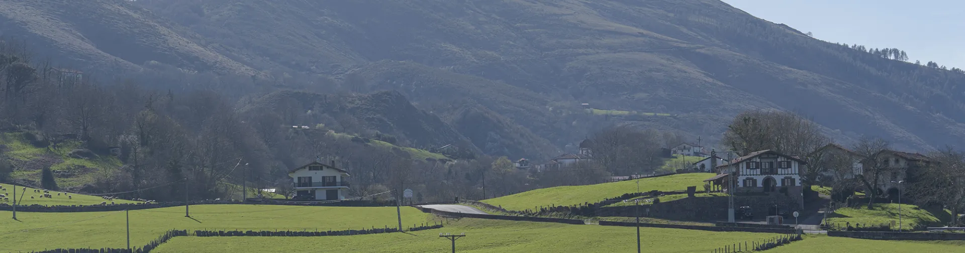 Valle de Xareta con prados verdes, caseríos tradicionales y montañas al fondo bajo cielo despejado.