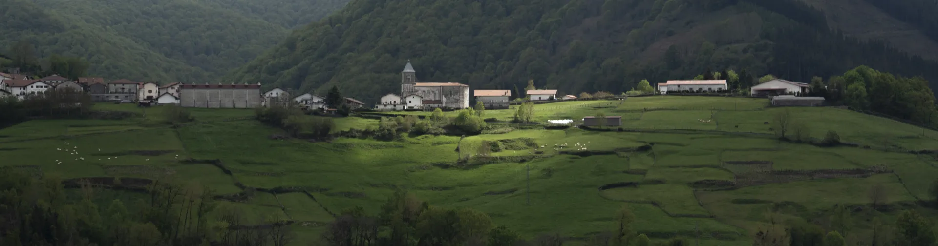 Montes boscosos y prados verdes rodean un pueblo en Plazaola-Sakana-Ultzamaldea.