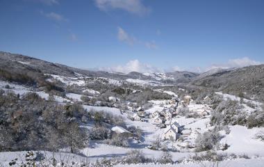 Pueblo de Abaurrea Baja en invierno con iglesia, casas de piedra blanca y montañas nevadas del Pirineo de fondo.