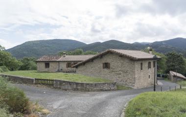 Casa rural de piedra en Antxoriz, Pirineo de Navarra, con jardín y montañas boscosas de fondo.