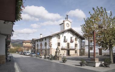 Plaza de Arbizu con iglesia de campanario, casas de piedra y arquitectura tradicional bajo cielo nublado.