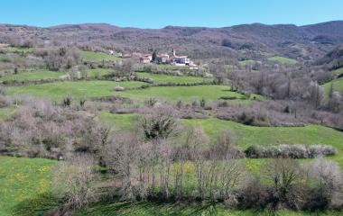 Pueblo de Arce en valle verde rodeado de montes boscosos y prados naturales.