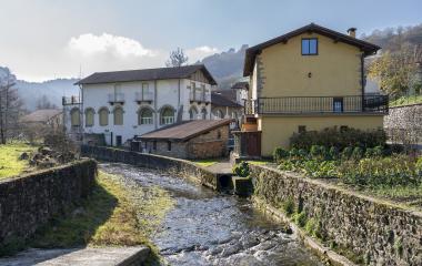 Casas tradicionales de piedra y estilo arquitectónico tradicional junto a río en Areso, con una huerta al lado.