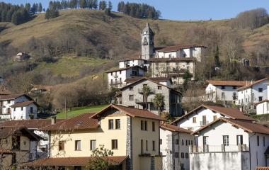 Casas tradicionales de piedra con iglesia de campanario en Areso, rodeadas de colinas boscosas.