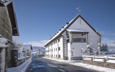 Señalización de entrada a Auritz-Burguete con escudos heráldicos cubiertos de nieve y paisaje pirenaico nevado de fondo.