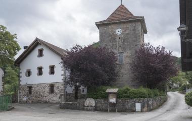 Iglesia parroquial de piedra en Azparren, Pirineo de Navarra, flanqueada por edificio de piedra y vegetación.