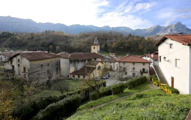Pueblo de Betelu con iglesia de campanario, casas de piedra con jardines y arbustos y rodeado de bosque y montañas.