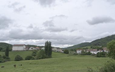 Vista general de Bizkarreta-Gerendiain con caseríos tradicionales, prados verdes y caballos en Pirineo navarro bajo cielo nublado.