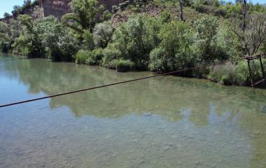 Cable histórico de la Barca de Monrealico sobre río con vegetación y bosque a los lados, situado en el Sendero Urdina.