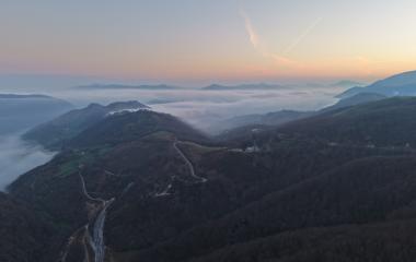 Vista de Belate cubierto de niebla al amanecer con carretera serpentante entre bosques.