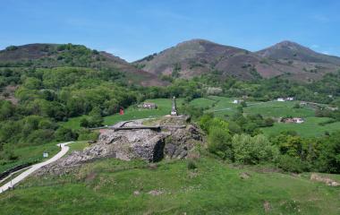 Castillo de Amaiur en valle de Baztan con monumento y paisaje de montañas verdes al fondo.