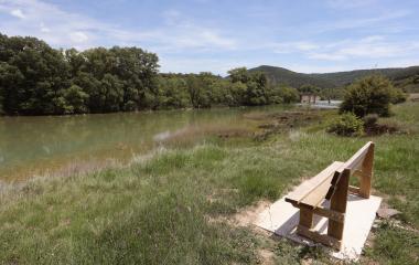 Banco de madera en orilla del río Aragón junto a zona de Coto de Pesca del Sendero Urdina, con vegetación y bosque.