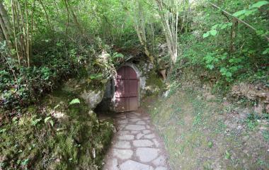Entrada de cueva con puerta de madera roja rodeada de bosque frondoso en Cuevas de Urdax, sendero empedrado.