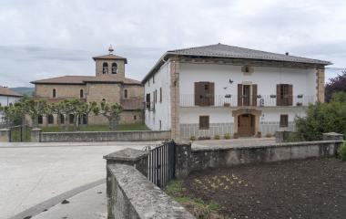 Calle de Esnoz con iglesia  de piedra y casa palacio blanca con balconada, en Pirineo navarro.