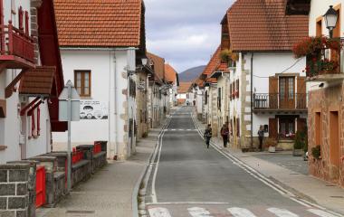 Calle principal de Espinal con caseríos tradicionales de tejado rojo, fachadas blancas y piedra con montañas al fondo.
