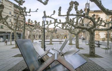 Plaza de Etxarri Aranaz con árboles podados y mobiliario urbano moderno, iglesia al fondo.