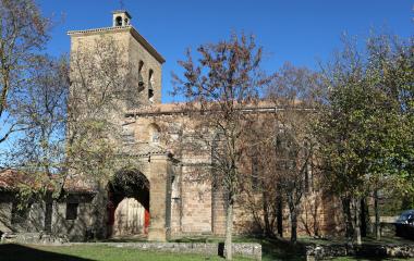 Iglesia de piedra con campanario en Ibargoiti, rodeada de árboles en tonos otoñales y vegetación local.