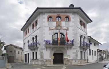 Ayuntamiento de piedra y ladrillo con balcones en Irañeta, con banderas y decoracion de glovos morados.