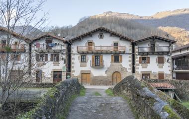 Vista de casas tradicionales vascas desde un puente de piedra y con montañas al fondo en Ituren.